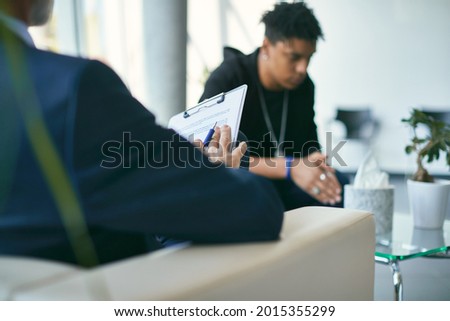 Close-up psychologist doing psychiatric evaluation on teenage boy during a session. 