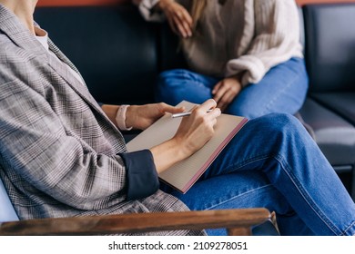 Close-up of a psychologist's hands writing down notes about a patient in a notebook. The psychologist makes a social survey of the reference group. A professional is talking to a client. - Shutterstock ID 2109278051