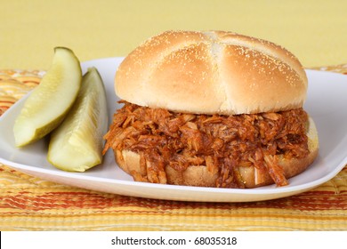 Closeup of a pulled pork barbecue sandwich with pickles on a plate