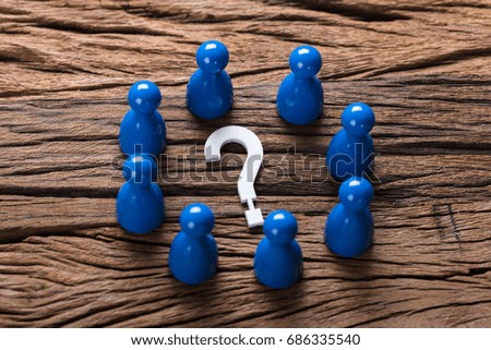 Closeup of question mark surrounded by blue pawn figurines on wood