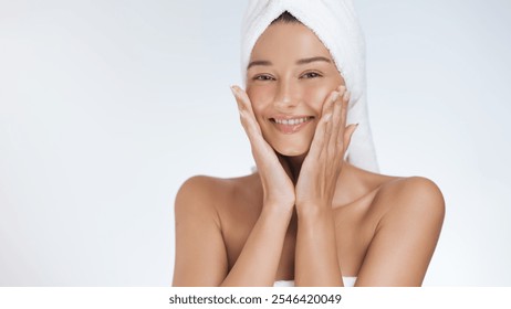 Close-up of a radiant woman with a towel turban, smiling and gently touching her face after a rejuvenating skincare routine. Perfect for promoting beauty, wellness, and self-care products in marketing - Powered by Shutterstock