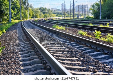 Closeup of the railroad tracks of a multi-lane railway stretching into the distance against the backdrop of a summer morning city on the horizon.