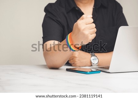 Close-up of a rainbow wristband in a hand while sitting at the table. Symbol of LGBTQ. Pride month. Gender diversity concept