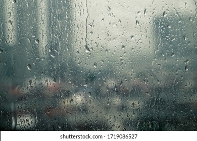 Closeup raindrops water droplets trickling down on wet clear window glass during heavy rain against blurred city view in rainy day monsoon season - Shutterstock ID 1719086527