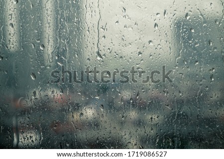 Closeup raindrops water droplets trickling down on wet clear window glass during heavy rain against blurred city view in rainy day monsoon season 商業照片 © 