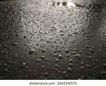 Close-up. Raindrops wet the surface of the table. The light in the distance creates reflections. The texture of the surface is clearly visible. Focus on the water droplets.
