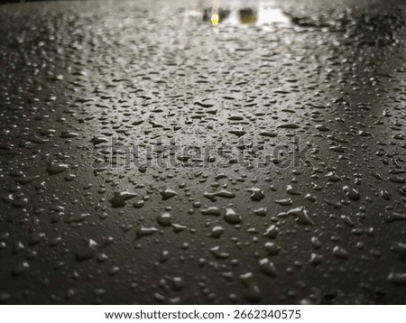 Close-up. Raindrops wet the surface of the table. The light in the distance creates reflections. The texture of the surface is clearly visible. Focus on the water droplets.
