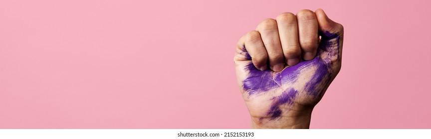 Closeup Of The Raised Fist Of A Man With Some Stains Of Purple Paint, On A Pink Background With Some Blank Space On The Left, In A Panoramic Format To Use As Web Banner Or Header