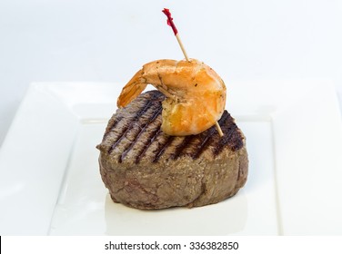 Closeup Of Rare Filet Mignon Topped With Shrimp On White Square Plate With White Background And Copy Space.