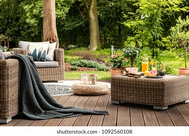 Close-up of rattan table with fruit and juice on it standing on a wooden patio in a spa facility garden