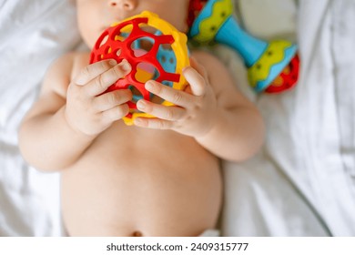 closeup rattle colorful toy in hand of infant kid. excited games with mom in nursery, biting First teeth concept. - Powered by Shutterstock