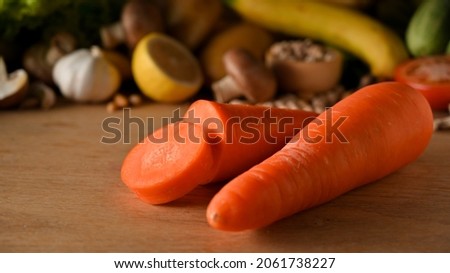 Close-up raw carrots and blurred various vegetables in the background on wooden board.  root vegetable, beta-carotene.