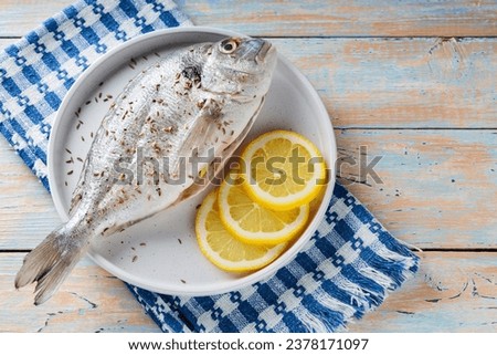 Close-up of raw dorado fish with lemon and cumin seeds on vintage wooden table