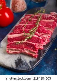 Close-up. Raw Meat Steaks With A Sprig Of Rosemary, Tomatoes On A Dark Blue Background. Recipes For Restaurant And Home Cooking. Banquet, Picnic, Family Holiday, Traditions.