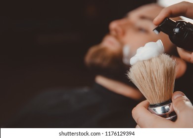 Close-up razor in hands of barber, background client is waiting for shaving his beard and mustache.