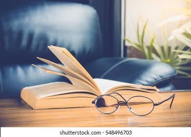 Closeup Of Reading Glasses With Open Book On Wood Table