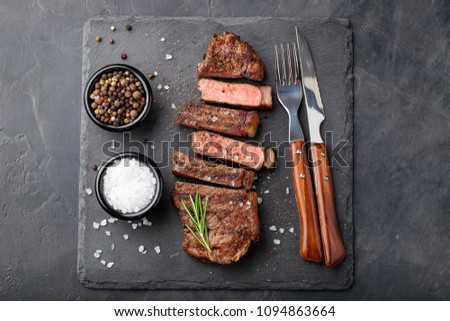 Closeup ready to eat steak new York beef breeds of black Angus with herbs, garlic and butter on a stone Board. The finished dish for dinner on a dark stone background. Top view