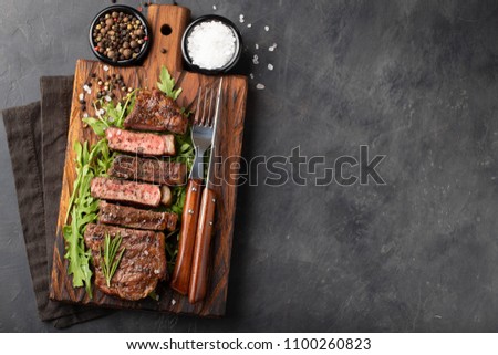 Closeup ready to eat steak new York beef breeds of black Angus with herbs, garlic and butter on a wooden Board. The finished dish for dinner on a dark stone background. Top view with copy space