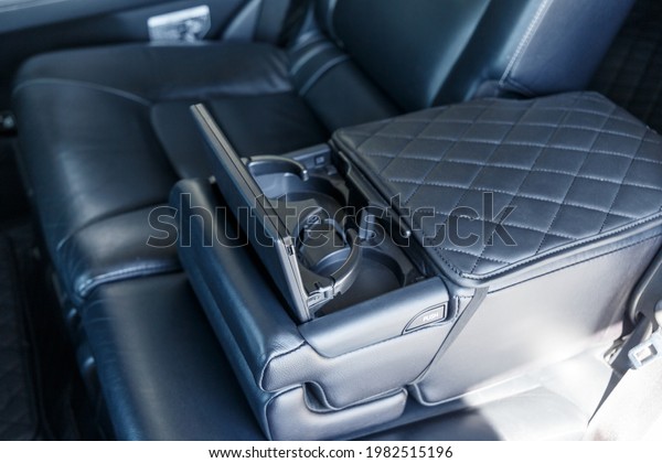 Close-up of the rear armrest with cup holders. The\
back row of an expensive car with an unfolded armrest. Car interior\
of luxury leather interior trim with white diamond stitching. Car\
detail