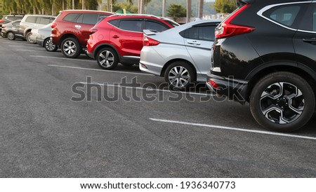 Closeup of rear, back side of black car with  other cars parking in outdoor parking area in bright sunny day.