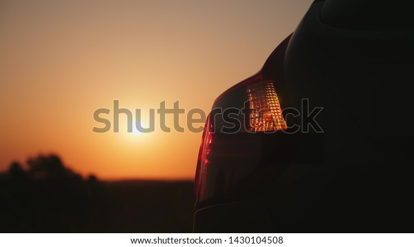 Closeup rear headlight of a car flashing\
emergency light on sunset\
background