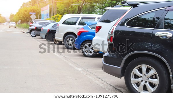 Closeup of rear side of black\
car and other cars park in parking area beside the street with\
natural background in sunny day. The way of transportation in the\
city.