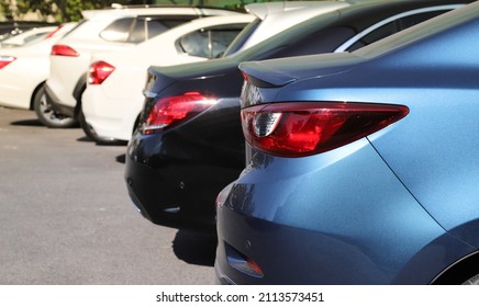 Closeup of rear side of blue sedan car with other cars parking in outdoor parking area in bright sunny day.