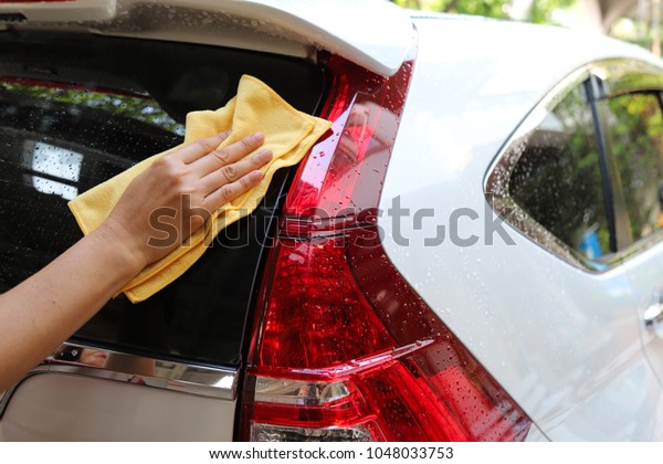 Closeup of rear side 
white car washing and cleaning  with yellow microfiber cloth by
woman's hand in sunny day. A simple work of family members, simply
way of life.