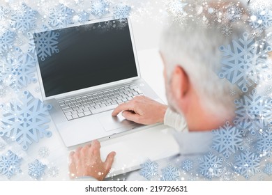 Closeup rear view of a grey haired man using laptop at desk against snow
