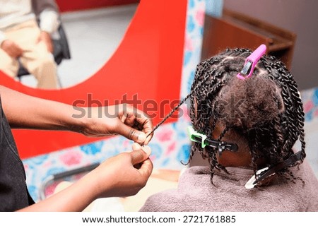 Close-up rear view of the hairstylist’s hands completing a braid on afro hair, highlighting skillful and precise work.