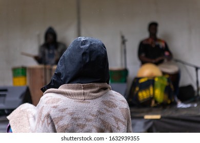 Closeup Rear View Of Person Wearing Raincoat And Listening Music Playing By Two Artists During Event In Rainy Season. At World And Spoken Word Festival