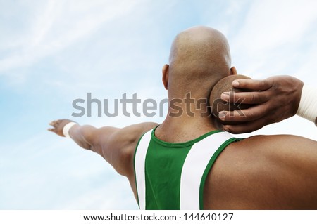 Closeup rear view of a shot putter preparing to toss shot put against the sky