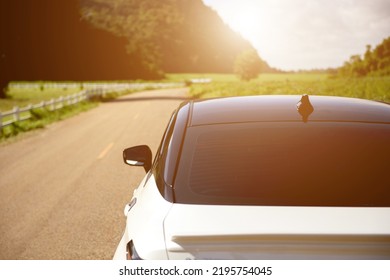 Close-up Rear View Of A White Car With Morning Light With Mountains And Sky On The Road.