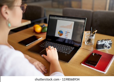 Close-up Rear View Of Young Business Or Student Woman Working At Cafe With Laptop Computer, Typing, Looking At Screen With Statistic, Using Touchpad. View Over The Shoulder. Telecommuting Concept.