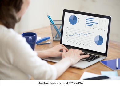 Close-up Rear View Of Young Business Woman Working In Office Interior On Pc On Desk, Typing, Looking At Screen With Diagrams. Office Person Using Laptop Computer In Office Workplace