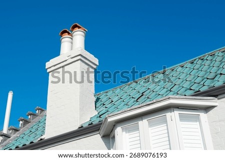 Close-up of a recently painted, brick work chimney showing the anti bird coverings. The teal coloured roof tiles and upper bay windows can be seen on a bright, sunny day in the UK.