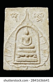 Close-up of a rectangular Thai Buddhist amulet with a raised seated Buddha figure inside an arched shrine, surrounded by leaf-like motifs and engraved script on an aged cream-colored surface.