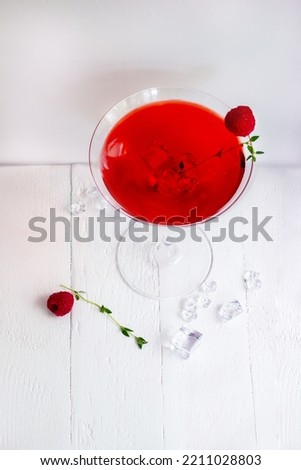 Close-up of red alcohol cocktail with raspberry and thyme on white wood table.