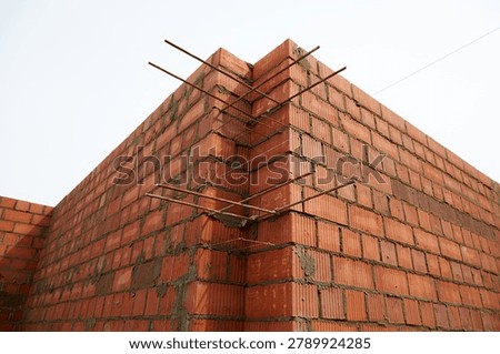 Close-up of a red brick corner wall with exposed reinforcement bars at an unfinished residential construction site. 