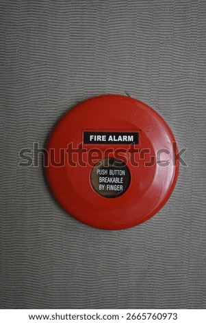 Close-up of a red fire alarm button mounted on a textured wall, with instruction text 