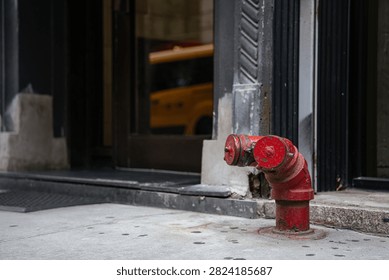 Close-up of a red fire hydrant mounted on a city sidewalk beside a building entrance. Urban concrete, doorway, and blurred yellow taxi create a realistic downtown street scene.