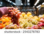 Closeup of red grape in a female hand at supermarket, woman looking for a grapes in a grocery store, female hand choosing grape in farm market, grocery shopping healthy lifestyle fresh fruits concept