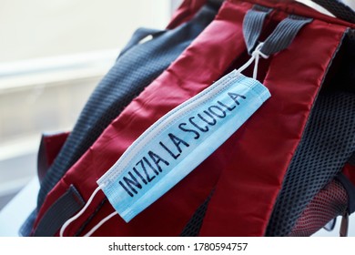 Closeup Of A Red And Gray Bookbag And A Blue Surgical Mask With The Text Back To School Written In Italian, Depicting The Need To Prevent The Infection At School In The Covid-19 Pandemic Situation