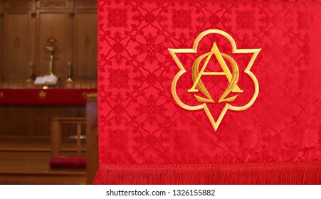Close-up of red lectern parament with  first and last letters of Greek alphabet in gold. Concept that God is the beginning and end of all things. Blurred altar, cross, Bible and candles in  background
