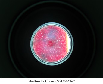 Close-up of red liquid under microscope viewed through glass lens, creating circular abstract scientific background.
