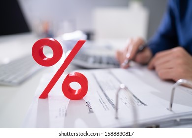 Close-up Of Red Percentage Symbol In Front Of Businessperson Calculating Invoice