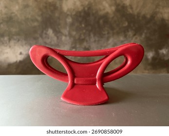 Close-up of a red plastic object with a unique curved design placed on a neutral background. The image shows an everyday household item, suitable for concepts of minimalism, design, or abstract shapes