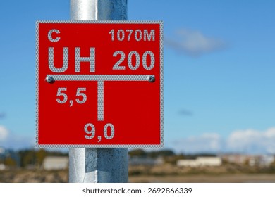 Close-up of a red reflective fire hydrant location information sign mounted on a galvanized metal pole against a bright blue sky background