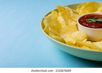 Close-up Of Red Sauce In Bowl Amidst Potato Chips Served In Plate On Blue Background With Copy Space. Unaltered, Unhealthy Food, Snack, Dipping Sauce, Crunchy, Salty Snack And Savory Food.