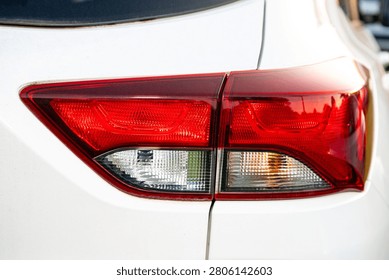 Close-up of a red tail light on a white vehicle, showing reflective plastic, brake light, turn signal, and rear car body detail.